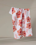 The Petal Paradise recycled kitchen towel by Whitney Urquhart, featuring a red and pink floral pattern, hangs on a clothesline against a neutral background.
