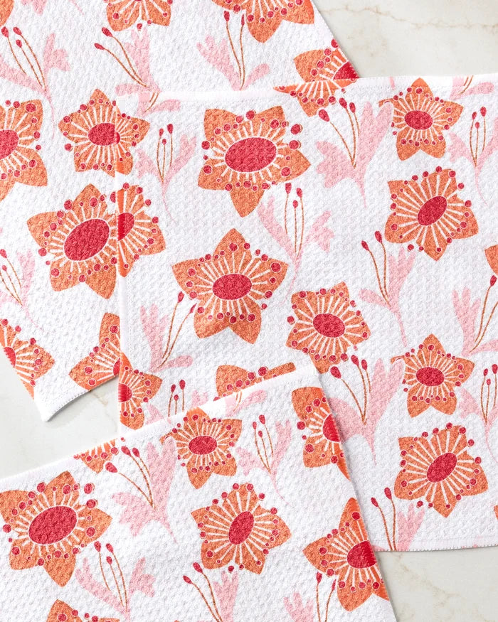 Four super-absorbent Whitney Urquhart Petal Paradise dishtowels, featuring vibrant red, pink, and orange floral patterns and textured surfaces, are arranged overlapping on a light countertop.
