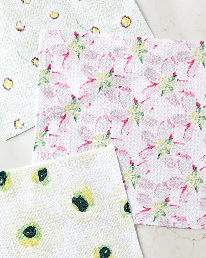Three Petals dishcloths by Ania Zwara Art, crafted from recycled materials, are arranged on a light surface: one with pink and green florals, another with yellow-green avocados, and the third with soft green-yellow dots.