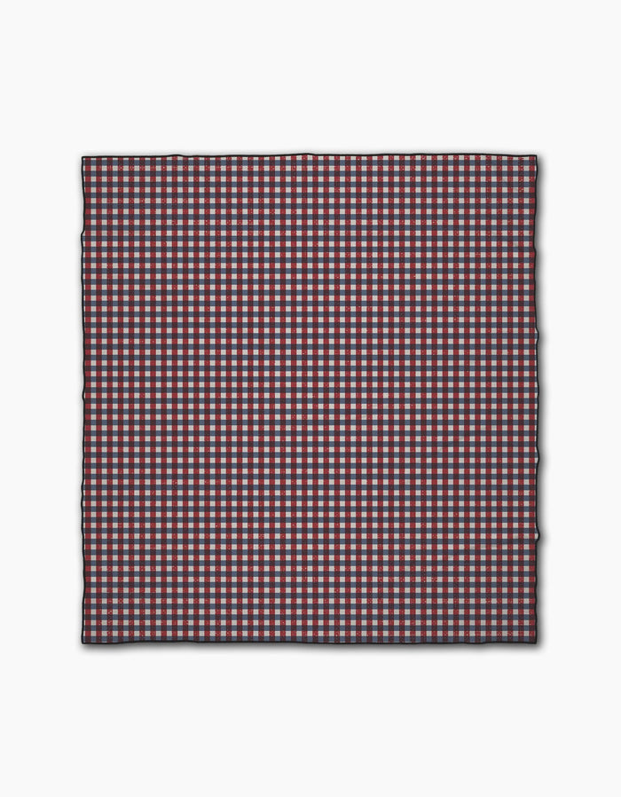 Geometrys Picnic Parade is a square cloth featuring a small red, white, and blue checkered pattern. Made from quick-drying recycled materials, it has neatly finished edges and is shown against a plain white background.