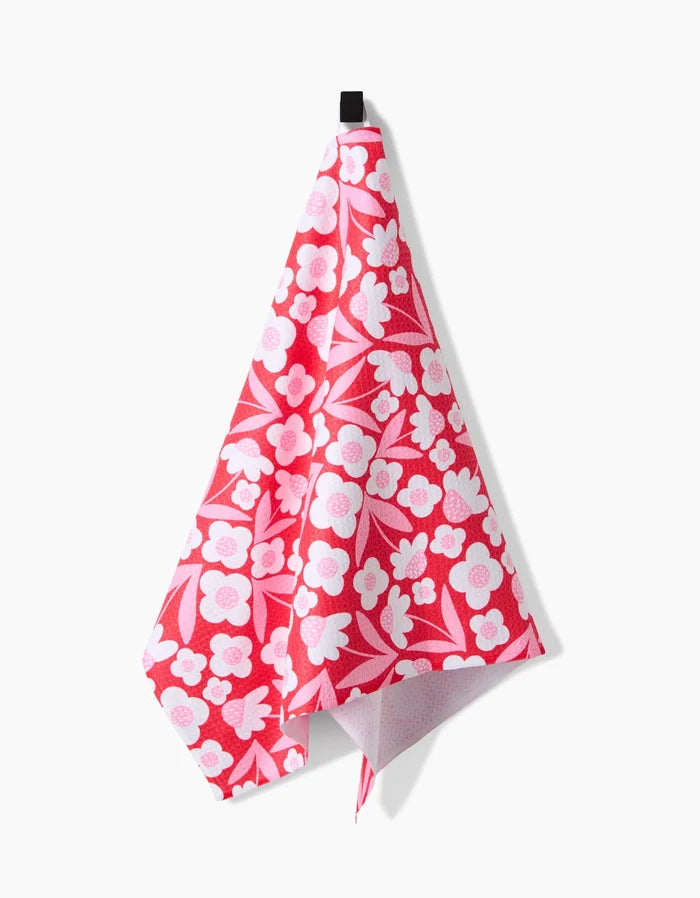 The Pink Blooms ultra-absorbent towel by Charlie Rowan Designs, featuring a pink and white floral pattern, hangs from a black hook against a white background.