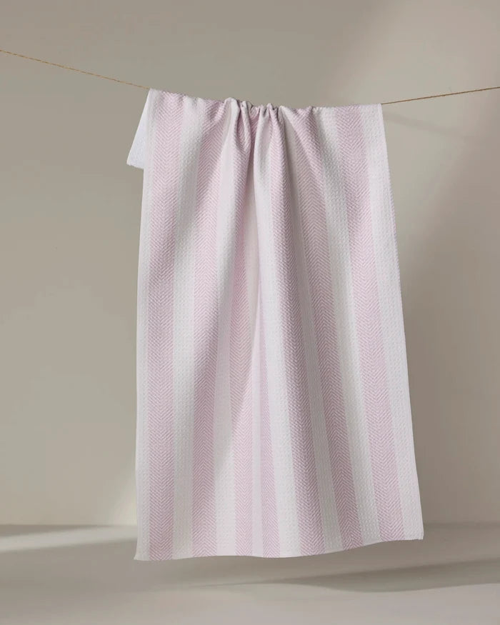 The Teri the Butter Pink Chevron Stripe ultra-absorbent towel hangs on a clothesline against a neutral beige background.