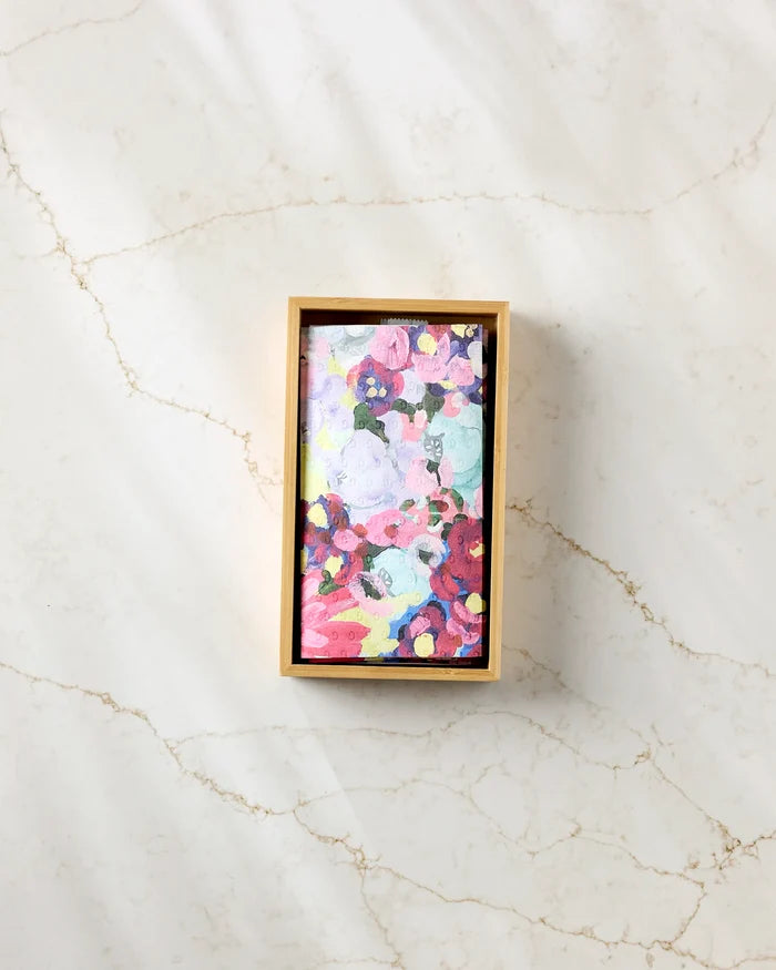 A rectangular wooden box holds "Pink Fields of Joy" by Ania Zwara Art, a colorful abstract painting with pink, purple, yellow, and blue shapes, displayed on a light marble surface next to eco-friendly paper towels.