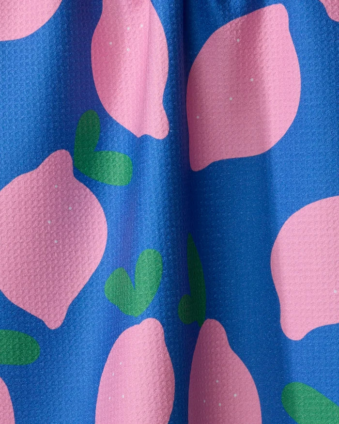 A close-up of the Jennifer Bouron "Pink Lemons" tea towel, featuring a textured surface and a vibrant pattern of large pink lemons and green leaves on a bright blue background, made from recycled materials.