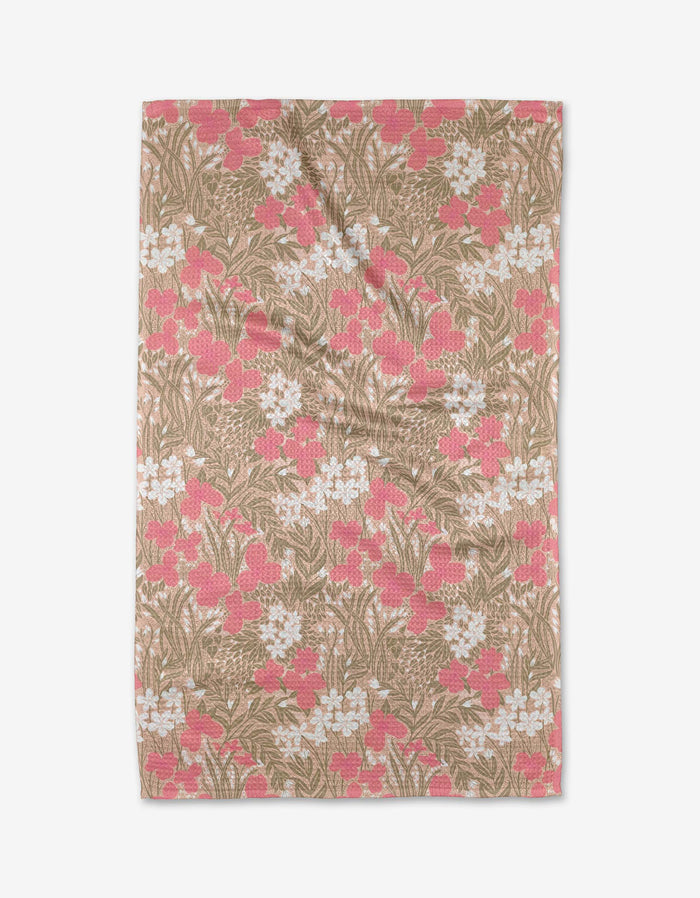 The Katie OShea Pink Meadow tea towel is rectangular, made from recycled materials, and features a floral pattern of white and pink flowers with green leaves on a light brown background.