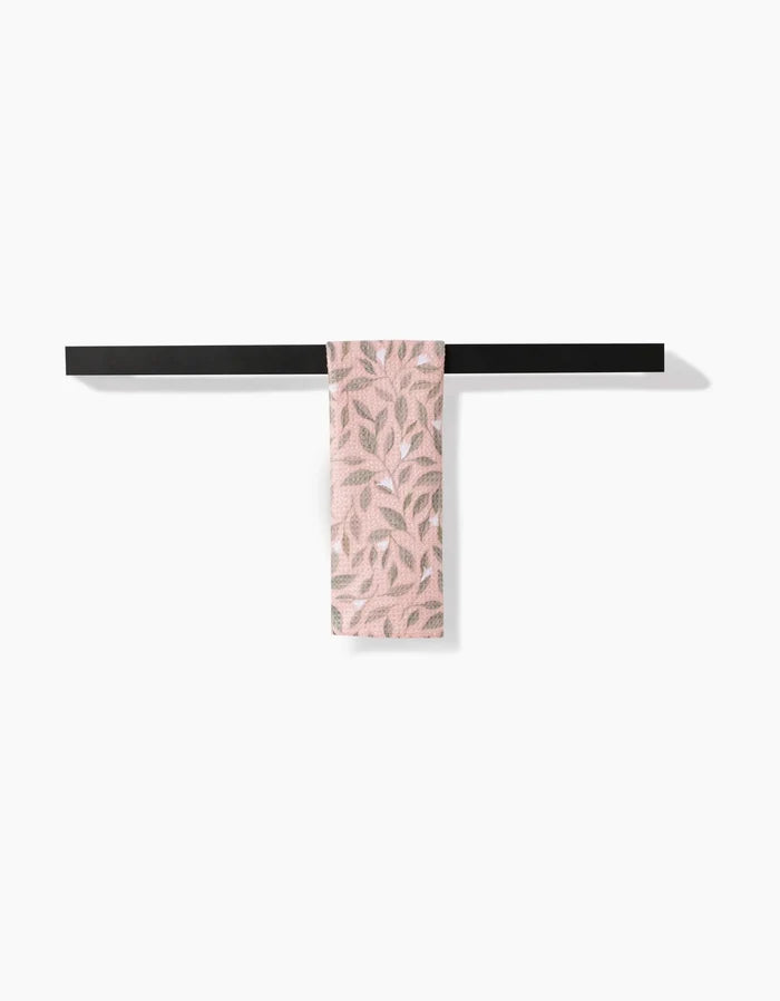 The Pink Mint Leaves bar towel by Katie OShea, featuring a leafy pattern and made from recycled materials, hangs on a black towel bar against a white background.