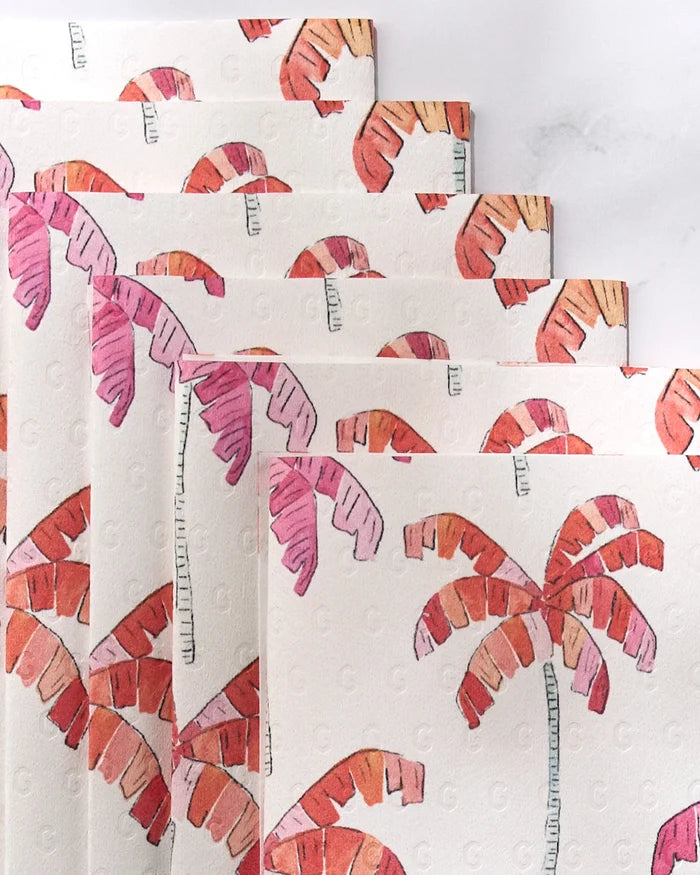 Pink Palms by GEOMETRY features white napkins with pink and orange watercolor palm trees, diagonally stacked. They offer a stylish, eco-friendly alternative to paper towels for sustainable entertaining.