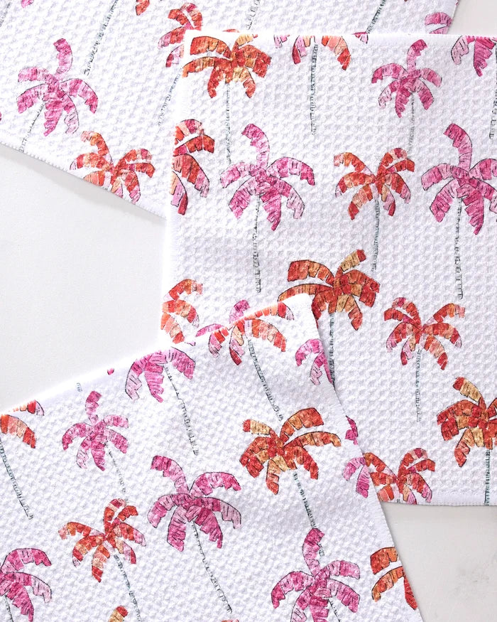 Three GEOMETRY Pink Palms napkins, made from recycled materials, feature a textured white base with repeating pink and orange palm trees. The overlapping napkins are arranged on a white surface for a vibrant, tropical vibe.