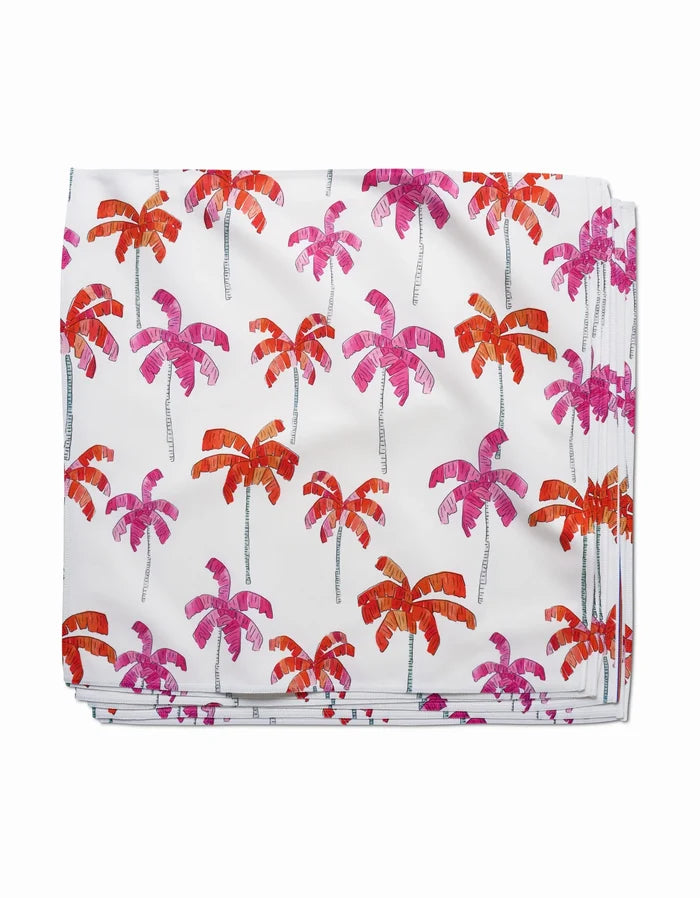 The Pink Palms dinner napkin by GEOMETRY is crafted from recycled Geosuede fabric, featuring a white base with a repeating pattern of red, orange, and pink palm trees with fine black trunks for sustainable style.
