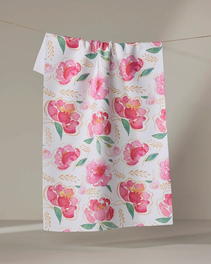 The "Pink Peony" tea towel by Elena Fay features a watercolor floral design with pink flowers, green leaves, and gold accents, displayed against a neutral background.