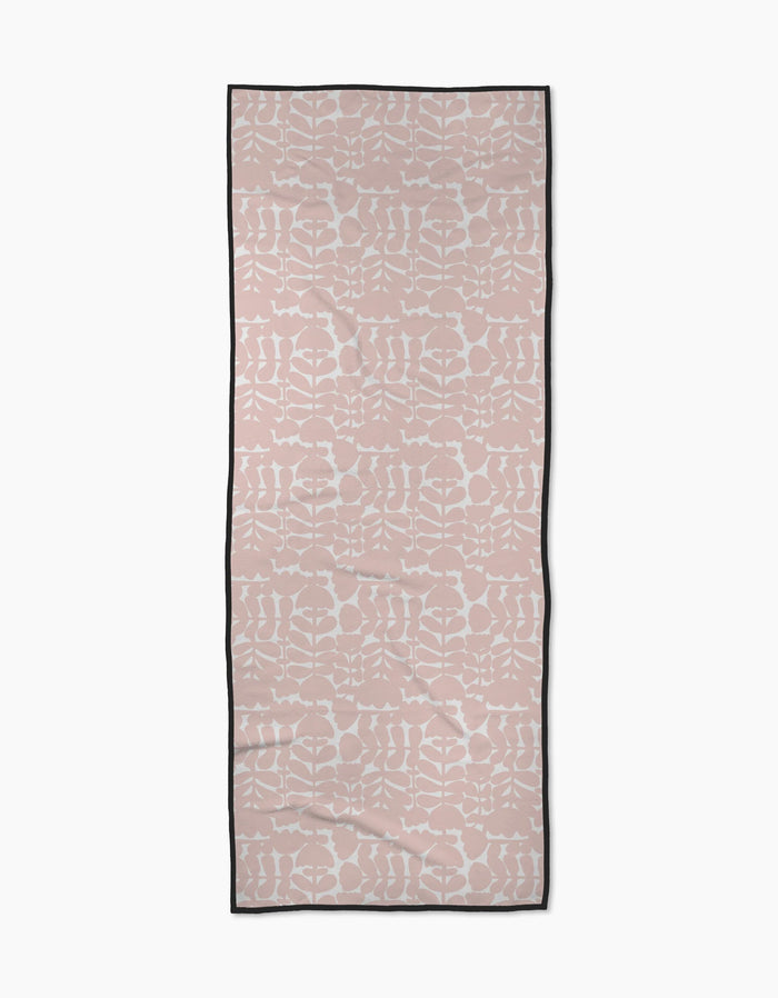 The Pink Scandi Flowers yoga towel by Katie OShea is rectangular, light pink with a white symmetrical floral pattern and a thin black border, shown flat on a white background.