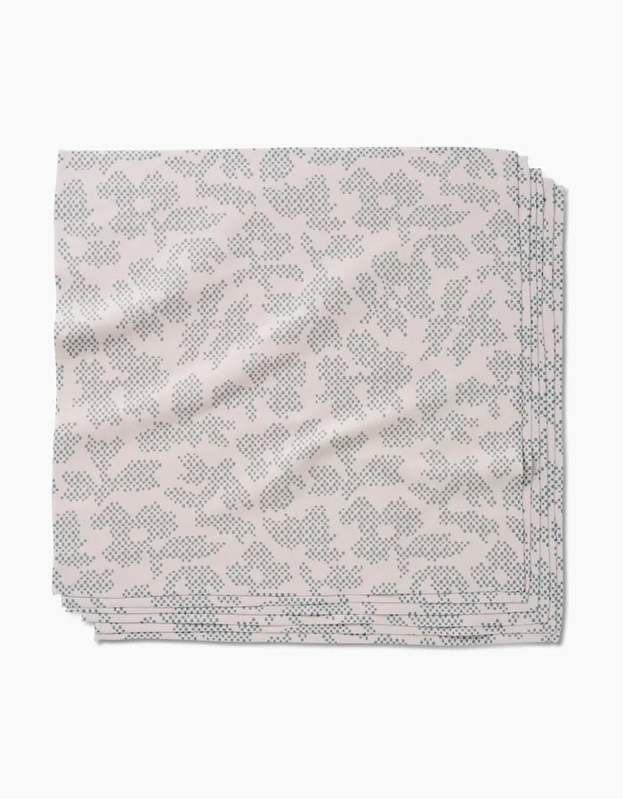 The Pixie Sage Dinner Napkin Set by Studio Jeannot features folded, light-hued Geosuede fabric with a subtle blue dotted floral pattern, elegantly displayed on a white background.