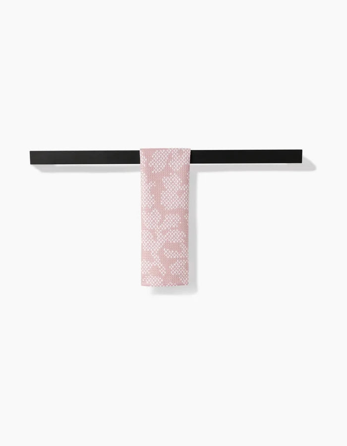 The Pixie bar towel by Studio Jeannot, featuring a pink and white pattern and made from recycled materials, is elegantly draped over a sleek black bar against a plain white background.