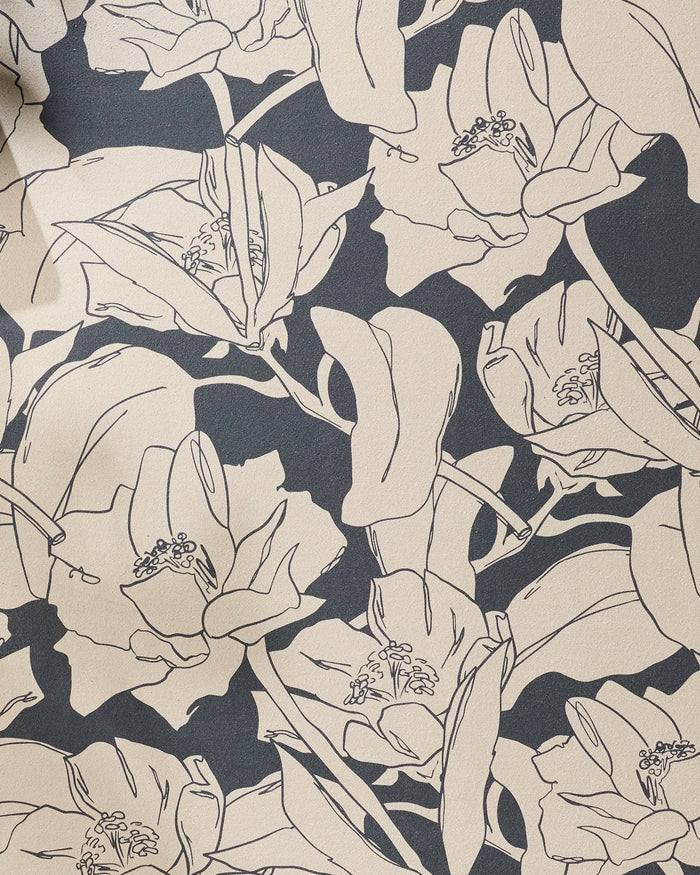 A close-up of Aubrey Fairchild's "Plant One on Me" wallpaper, featuring a beige background with black line drawings of large, detailed flowers and leaves in a repeating pattern inspired by recycled yoga towels.