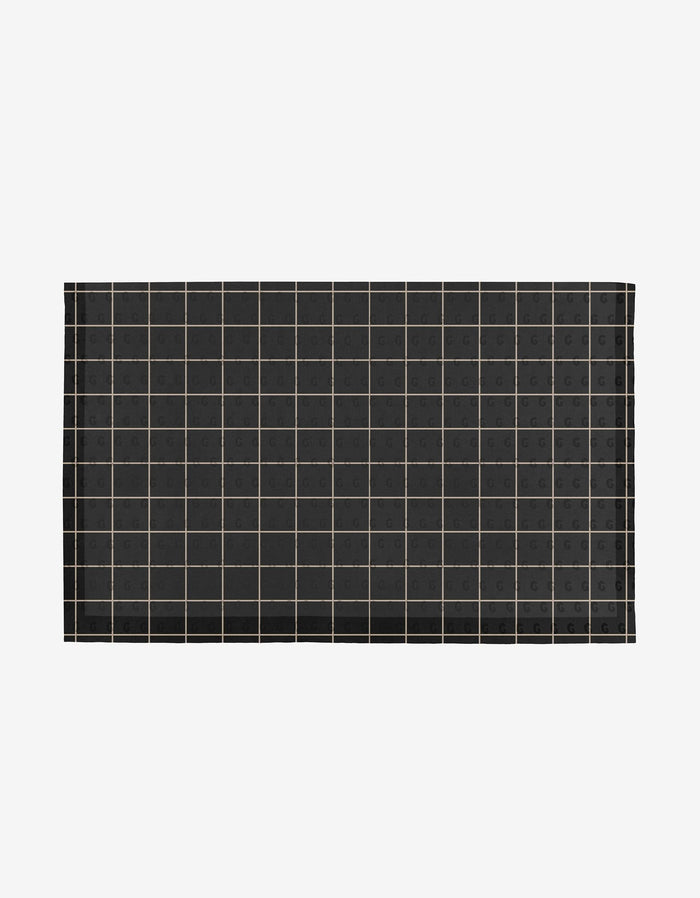 The Plant One on Me mat by Aubrey Fairchild is a rectangular black mat with a grid of thin light lines and small G symbols in each square, made from eco-friendly post-consumer recycled materials. Displayed on white. Not Paper Towels.