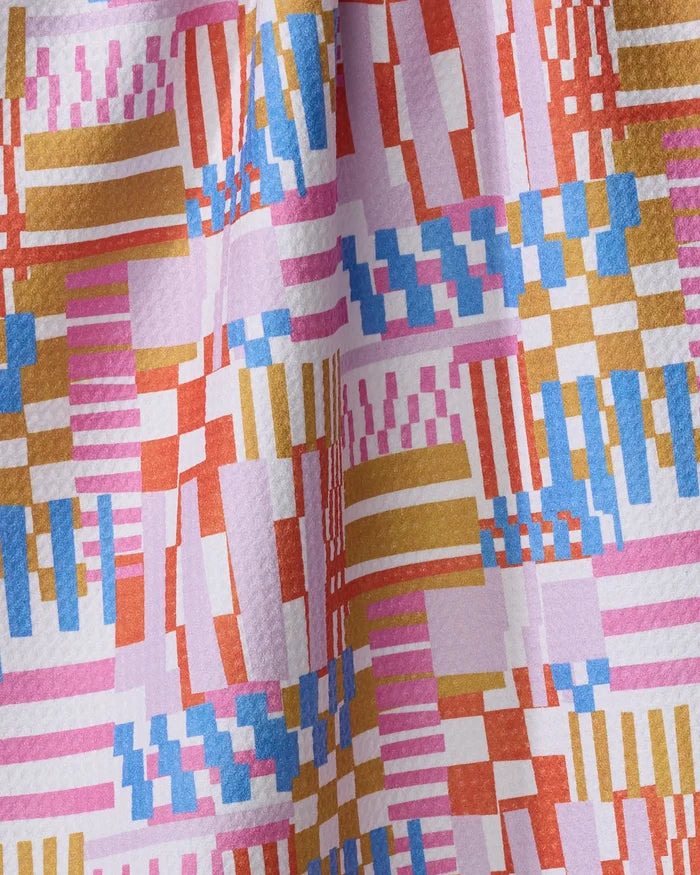 A close-up of the Playful Stripes quick-drying towel by Claire Iglesias, showcasing its geometric pattern in pink, blue, gold, orange, and white with subtle texture and gentle draping.
