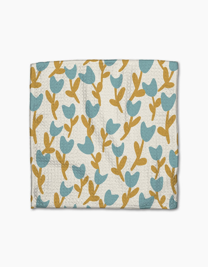 Introducing Polka Dot Blooms by Lizzie Clark—a wallet with a textured surface, adorned with blue tulip-inspired flowers and mustard stems on white, capturing the whimsical charm of super-absorbent recycled dishcloths.