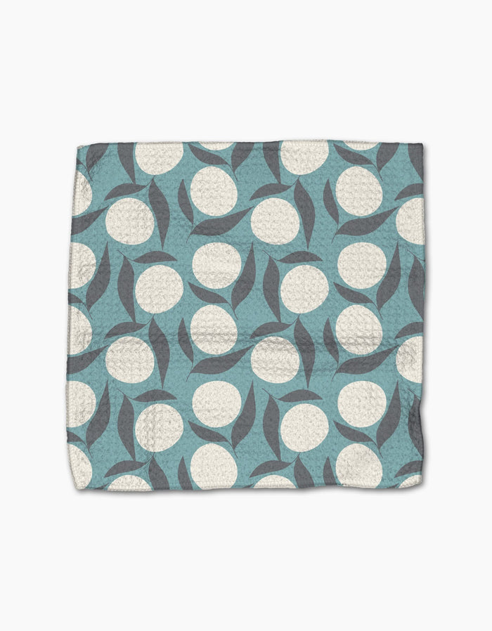 The Polka Dot Blooms quilted dishcloth set by Lizzie Clark is made from recycled materials and features a blue background with white circles and overlapping gray leaves.
