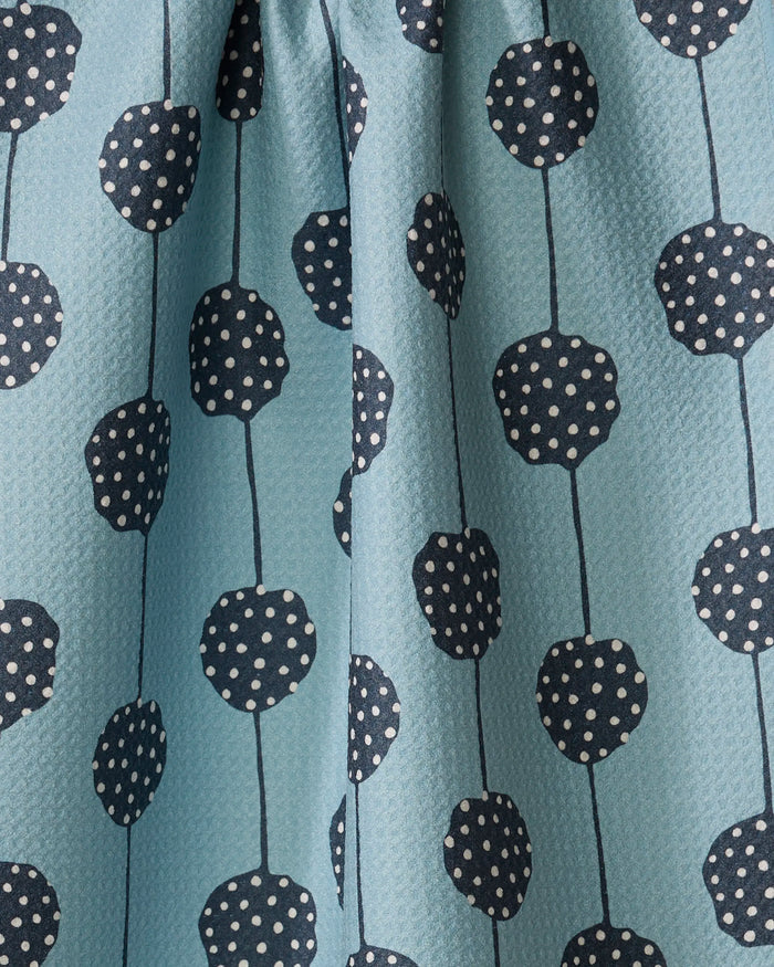 Close-up of Lizzie Clark's Polka Dot Garland, an eco-friendly light blue kitchen towel with textured fabric, featuring dark blue vertical lines topped with circle accents filled with white polka dots.