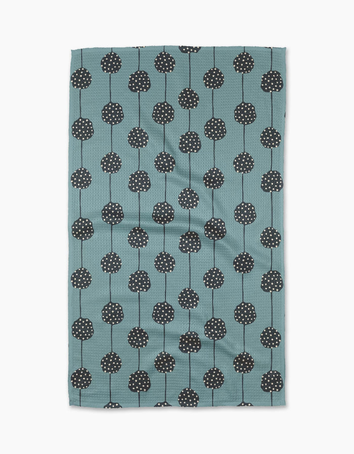 The Polka Dot Garland tea towel by Lizzie Clark is made from recycled materials in teal, with a pattern of black round flowers with white dots and thin stems arranged in vertical rows. The slightly wrinkled fabric is displayed on a white background.