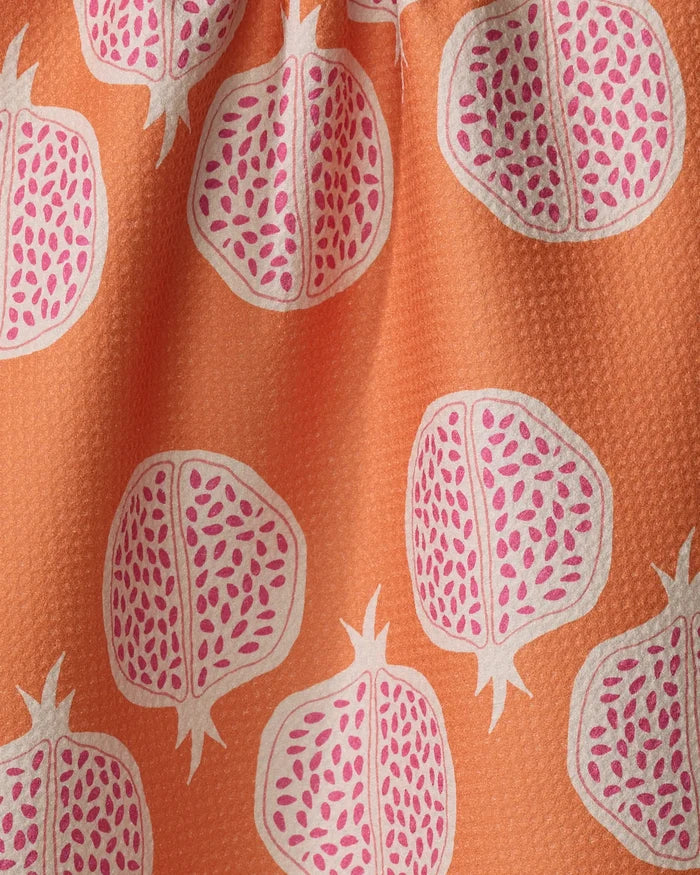 The Pomegranate Parade kitchen towel by Lizzie Clark features orange fabric with white and pink pomegranates, split to reveal seeds. Its slightly textured surface and gentle folds add charm to any space.