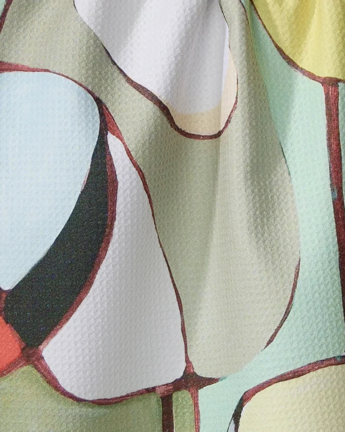 The “Poppies on Mint” tea towel by Rachel Austin features an abstract, multicolored pattern in pale green, white, black, red, and beige. Made from recycled materials, it’s quick-drying and adorned with curved, interconnected shapes for visual interest.
