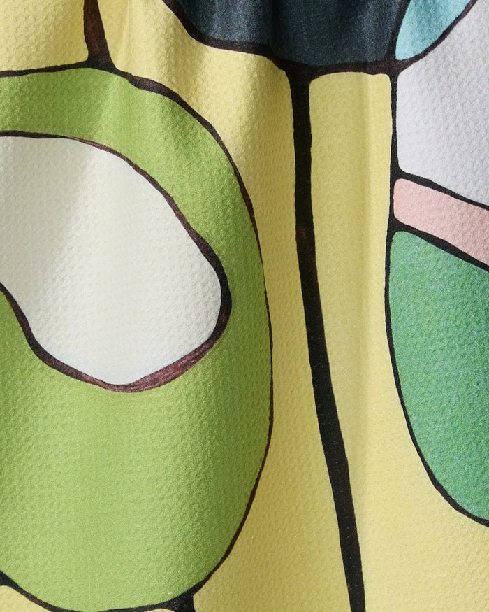 Close-up of "Poppies on Yellow" recycled kitchen towel by Rachel Austin, featuring a colorful abstract pattern—green, white, black, and pale yellow shapes outlined in black—with visible fabric texture.
