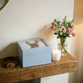 Blue Pet urn on a shelf with a candle and flowers and dog collar.