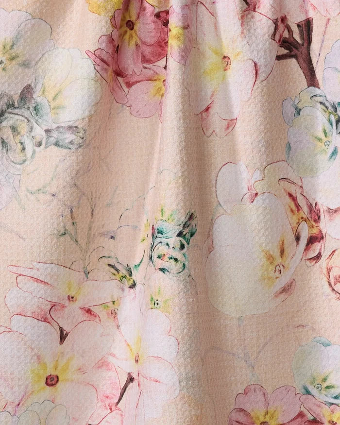 A close-up of the 'Primroses' fabric by Pascale Dilger, showing large pastel pink, yellow, and white flowers with green leaves on a beige background—perfect for a charming recycled tea towel.