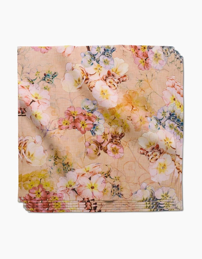 Primroses by Pascale Dilger is a square, eco-friendly napkin featuring a pastel peach background with watercolor-style pink, yellow, purple, and green floral designs—a charming spring addition to your dinner napkin collection.