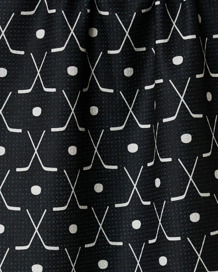 Close-up of the GEOMETRY Puck tea towel with ultra-absorbent black fabric, featuring a repeating grid pattern of white crossed hockey sticks and pucks for a sporty look.