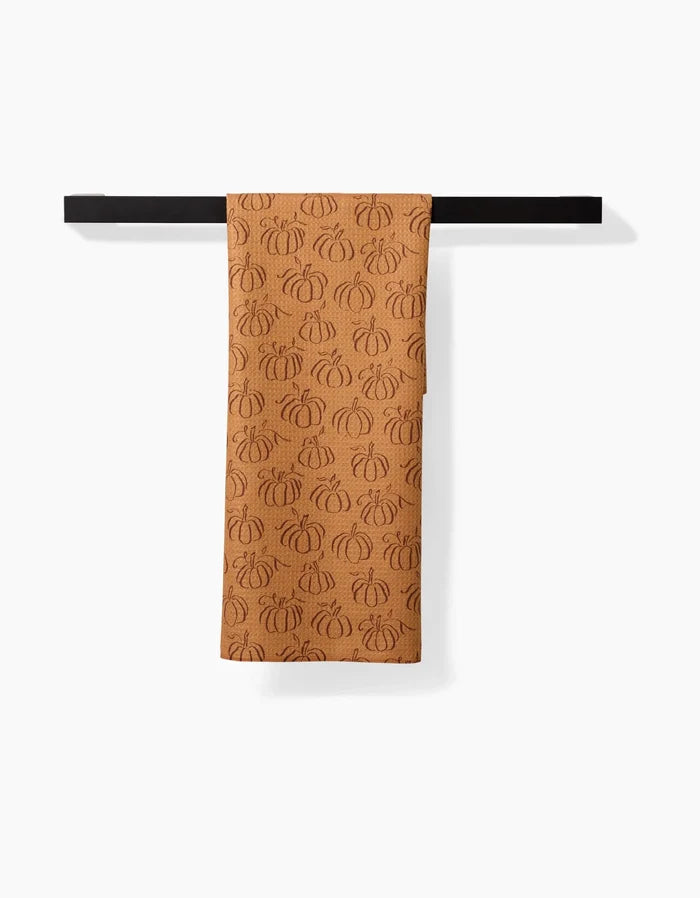 The Pumpkin Patchwork recycled kitchen towel by Aubrey Fairchild, featuring outlined pumpkins, hangs neatly over a black towel bar against a white background.