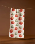 The Geometry Pumpkin Pop towel, ultra-absorbent and white with green and orange pumpkin patterns, hangs by two clothespins on a string against a brown background.