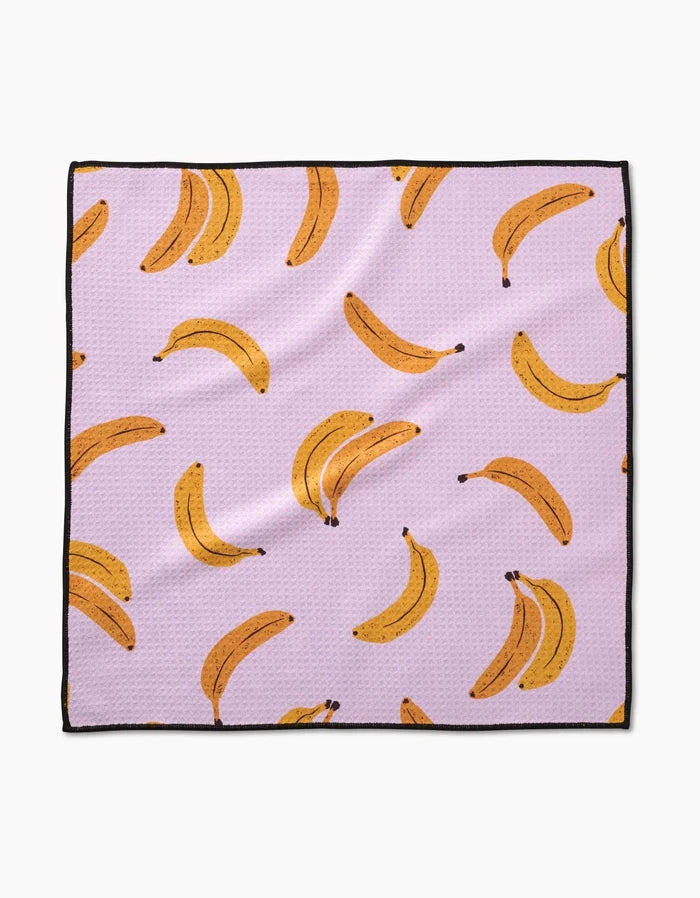 The Geometry Pupnana is a square Paw Towel with a light purple background, repeating yellow banana illustrations (single and in pairs), ultra-absorbent Geoweave fabric, and a sleek black border around the edges.