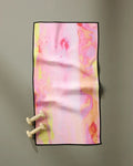 The GEOMETRY Purity towel, ultra-absorbent and fast-drying with pastel pink, yellow, and orange abstract patterns, lies flat on a gray surface. Two small beige dumbbells rest in the bottom left corner.