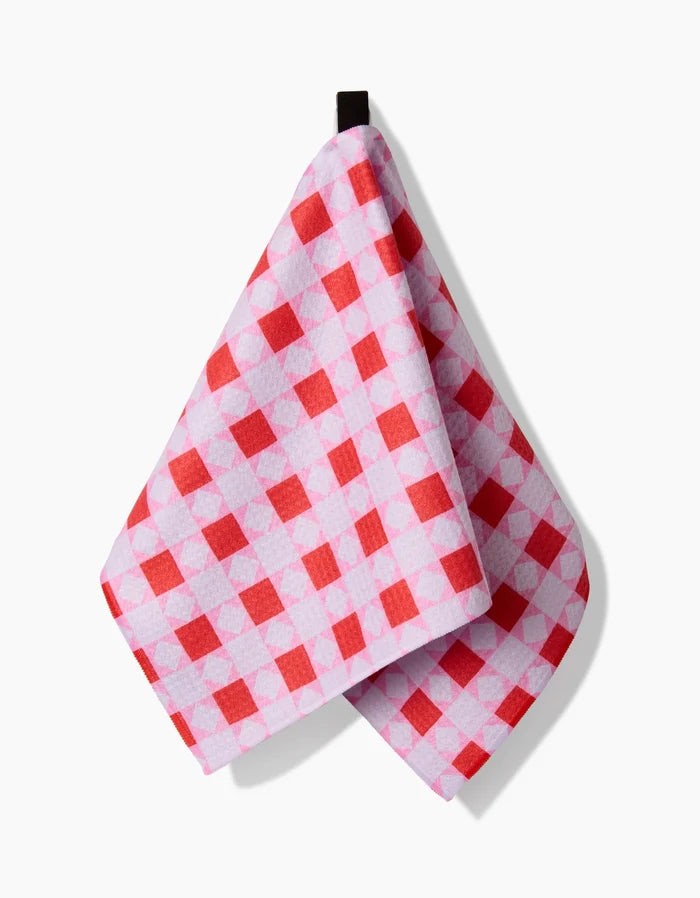 The Quilt Block Pink Andred bar towel by Brittany Jepsen, made from Geoweave fabric with a red and white checkered design, hangs from a black loop against a white background.