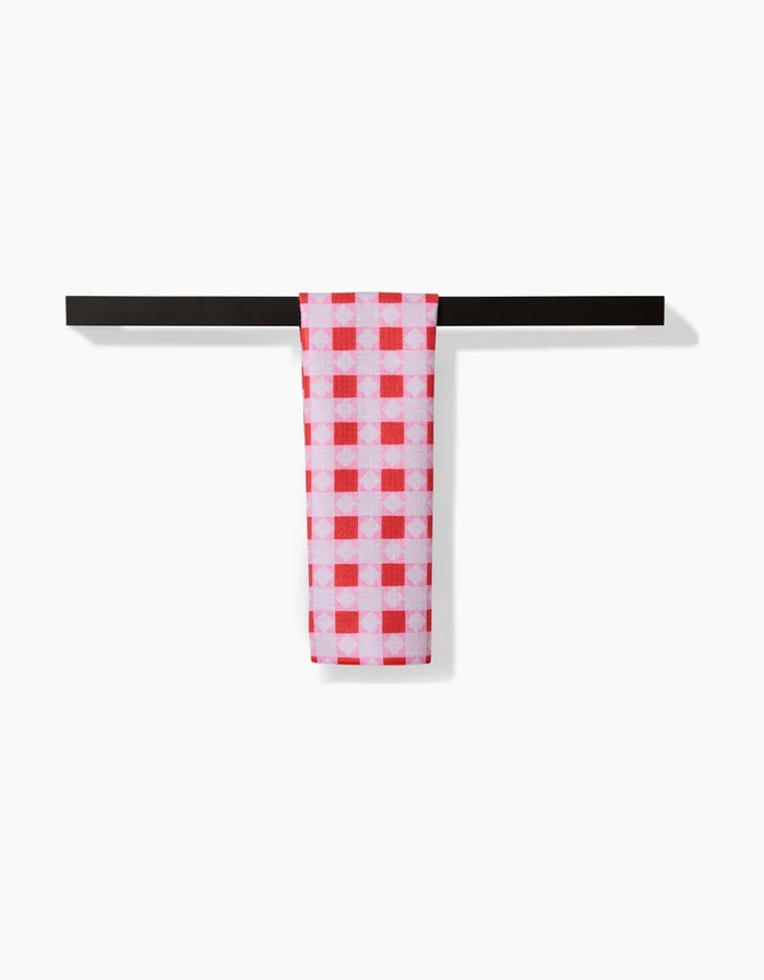 The Quilt Block Pink Andred bar towel by Brittany Jepsen, featuring a red and white checkered Geoweave fabric, hangs neatly over a simple black bar against a plain white background.