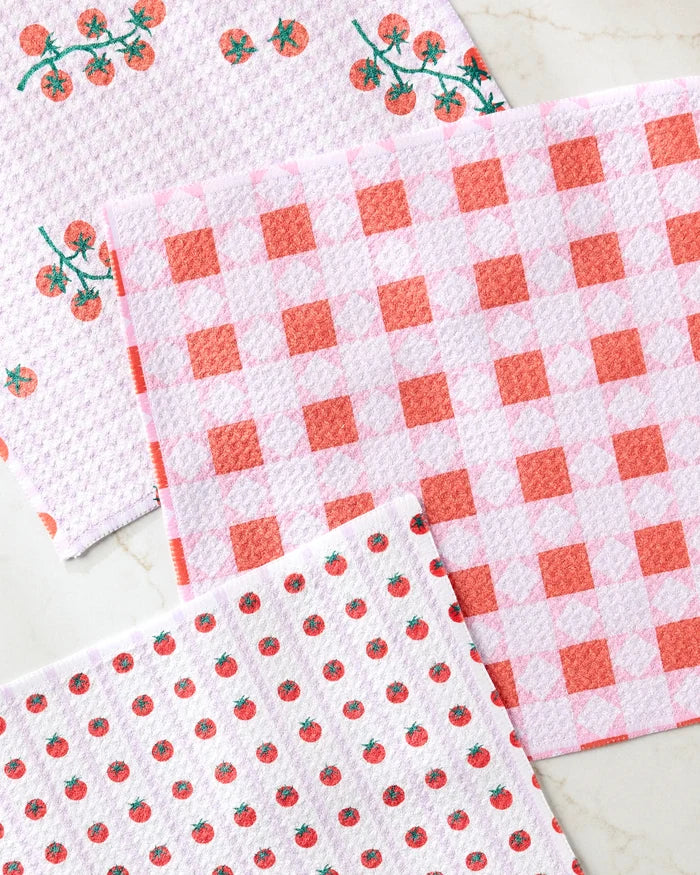 Three super-absorbent Brittany Jepsen Quilt Tomato Harvest dishtowels, featuring tomato prints, red and white checks, and embroidered tomato vines, are displayed on a marble surface.