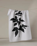 A PrintedPlant "Raspberry" white tea towel featuring a bold black botanical silhouette hangs on a thin clothesline against a neutral background.