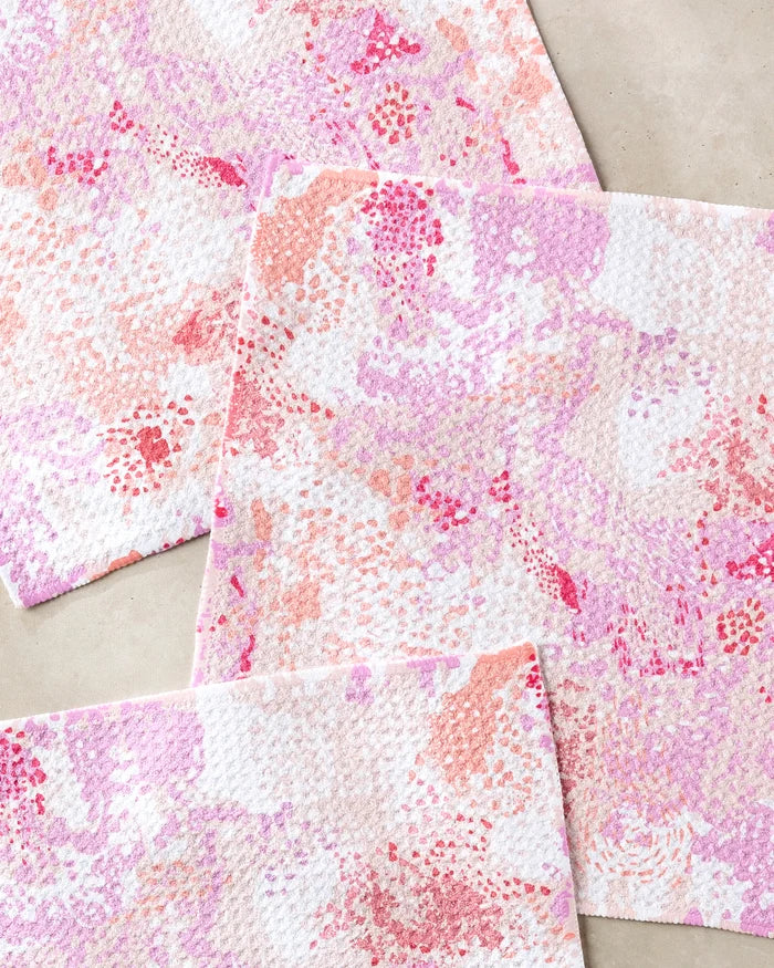 Three absorbent Rawhide dishcloths by Elisabeth Wing, featuring a pink, red, and purple abstract pattern, are laid out with overlapping corners on a light beige surface.