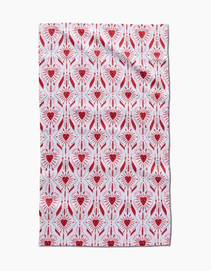 The Ray of Love tea towel by Roxy Marj features a rectangular, quick-drying white background with vertical rows of red and pink geometric heart and eye motifs, creating a symmetrical, evenly spaced design.