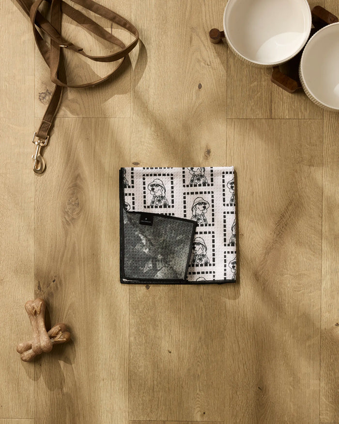A flat lay features Geometry's Ready For Summer Doggy set: a leash, patterned bandana, ultra-absorbent dog towel, bone-shaped toy, and two white bowls on a wooden stand.