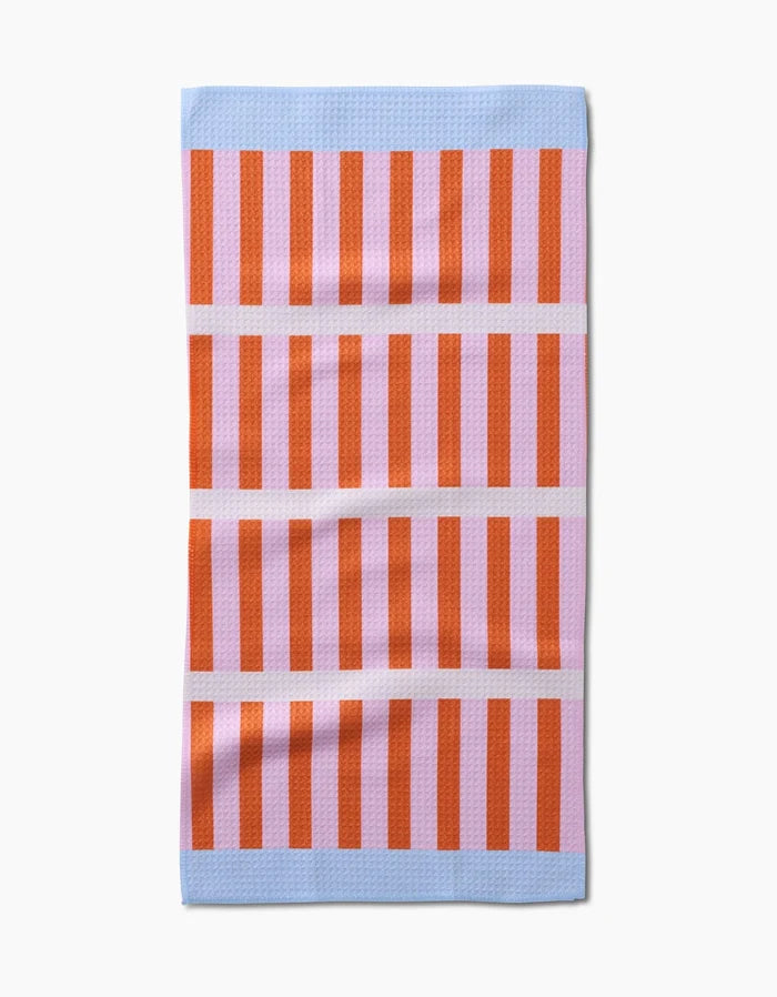 The Red Glow Bar Towel by Happy Hemera features vertical red and pink stripes with light blue bands at the top and bottom, separated by three pink lines. Made from Geoweave fabric, it lies flat on a white background.