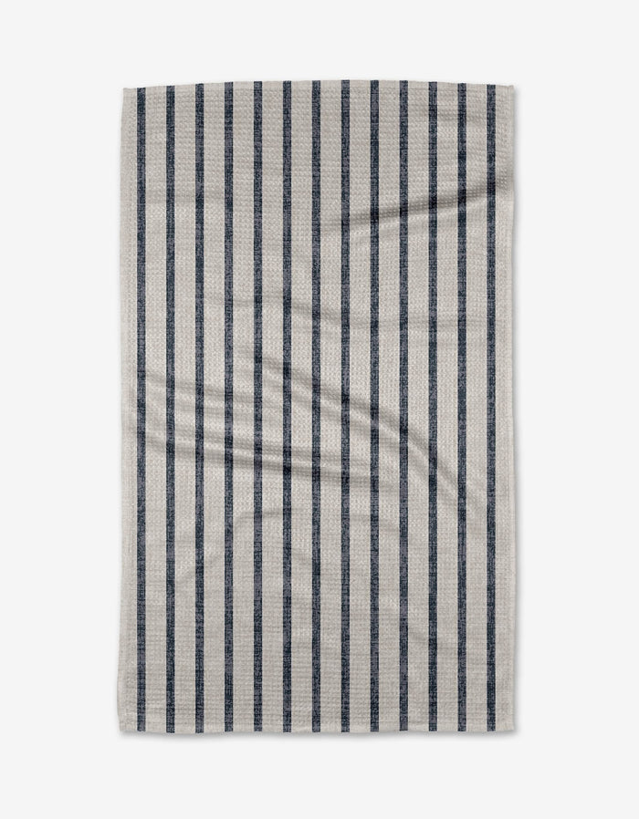 A rectangular beige Becki Owens Ren Blue tea towel, made from ultra-absorbent Geoweave fabric, features evenly spaced dark blue vertical stripes and subtle wrinkles, displayed flat on a white background.