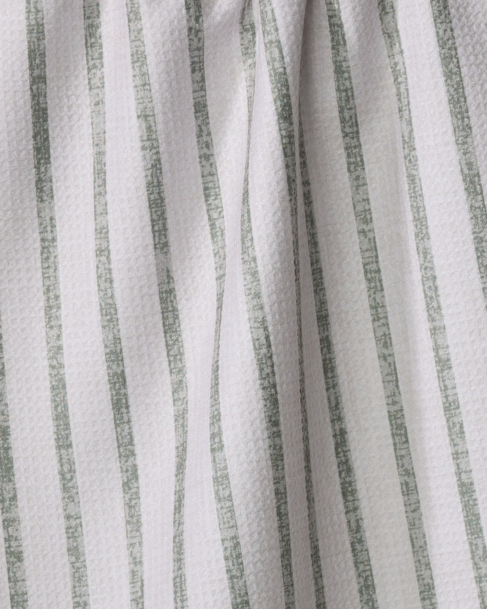 A close-up of the Becki Owens Ren Sage tea towel shows its white, textured fabric with vertical, irregular green stripes, gently wrinkled for soft folds and subtle shadows.