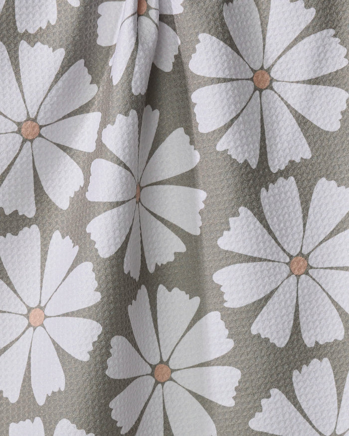 The Retro Daisy kitchen tea towel by Hufton Studio features a textured, slightly wrinkled fabric made from recycled materials, and showcases a repeating pattern of large white daisy-like flowers with light brown centers on a muted gray-green background.