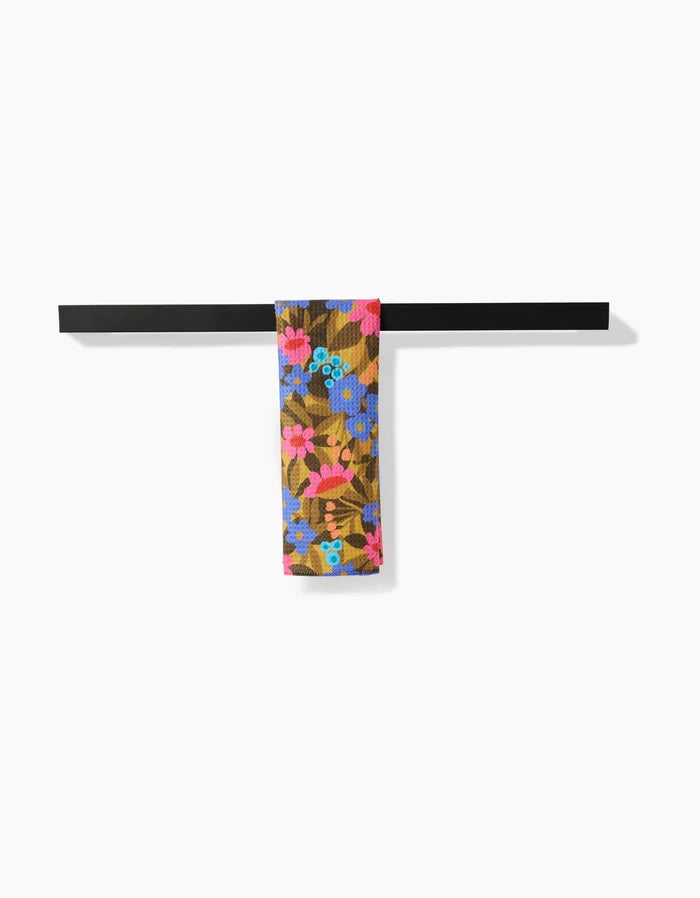 The Lisa Nelson Retro Garden Bar Towel, featuring a colorful floral pattern and made from recycled materials, hangs neatly over a horizontal black metal bar against a plain white background.