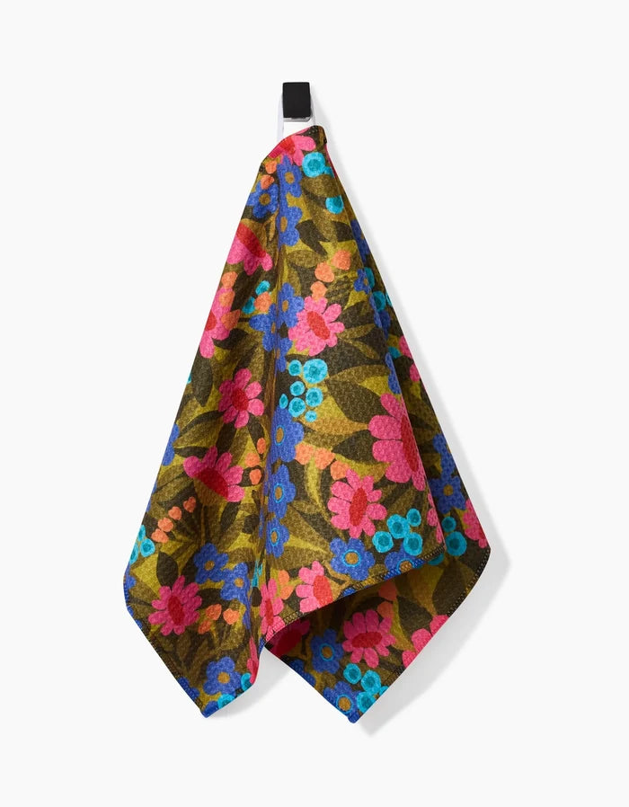 The Lisa Nelson Retro Garden Bar Towel features a vibrant floral pattern with blue, pink, and red flowers plus green leaves on durable Geoweave fabric, displayed hanging from a black loop against a white background.