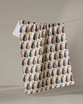 The Megan Kampa "Retro Pears" kitchen tea towel, made from recycled materials, features a navy blue, beige, and muted orange abstract pear pattern. It hangs from a string against a light background.
