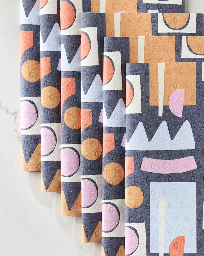 Claire Iglesias’ Retro Shapes Fiesta folded reusable paper towels showcase abstract blue, orange, pink, and white patterns—circles, rectangles, and zigzags—laid on a marble surface as an eco-friendly kitchen towel option.